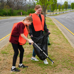 Two teens smile as they collect litter from the grass.